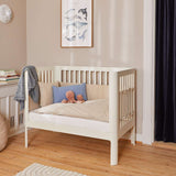 Cream FLEXA Baby Bed, 140x70cm, wood, with pillows and toys in a softly lit nursery with child-safe rounded edges.