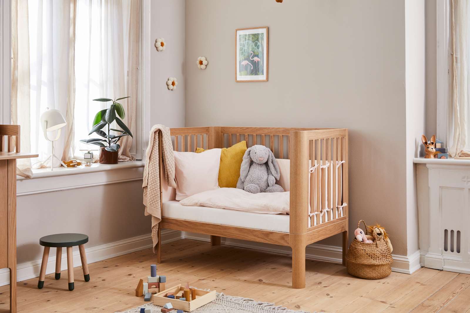 FLEXA BABY oak cot bed in a neutral nursery, soft bedding and child-safe rounded edges visible.