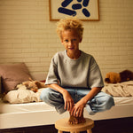 Child with curly hair sits on FLEXA DOTS stool in blushing pink, child-safe design, in a modern, cosy childrens room.